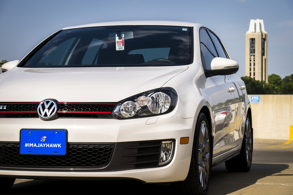 Front view of white VW sedan parked with Campanile in the background.