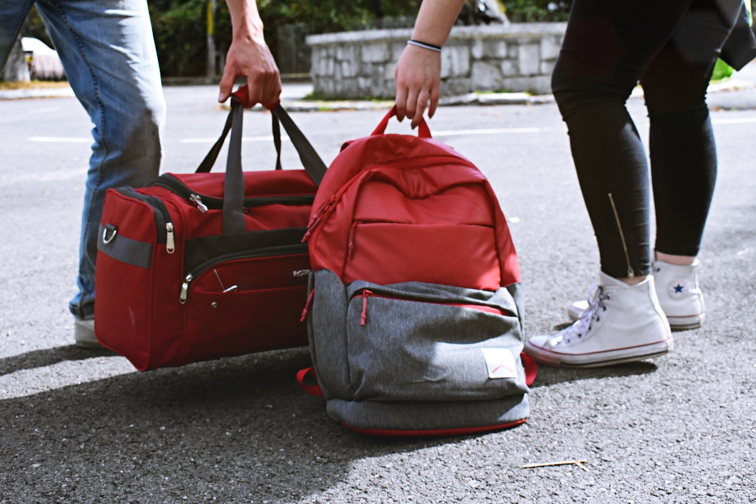 Waist down view of male and female picking up a duffle bag and backpack.